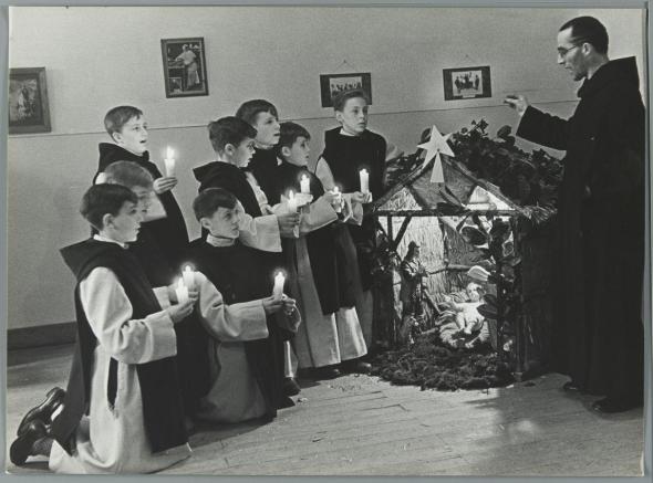 A Monk conducts a Christmas choir of boys dressed in religious robes to sing Christmas carols beside a nativity display. Bruges, 1935 Courtesy Flickr Commons